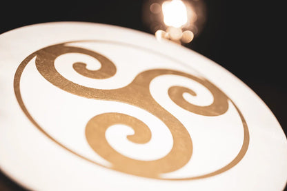 16-inch hand drum with Triskele design by Utah Energy Healing Center, shown in a lifestyle setting with natural wood finish.
